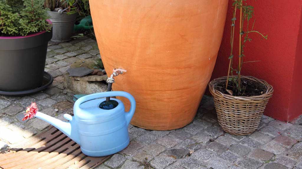 Garten-Fibel - einer Regentonne, die wie eine Terrakotta-Amphore aussieht, wird Wasser entnommen