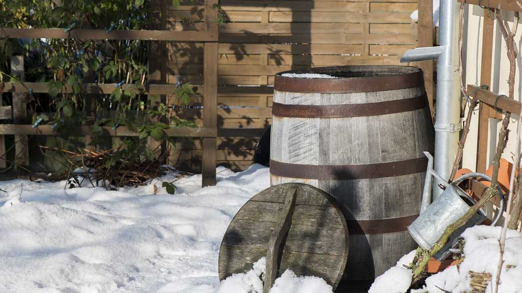 Garten-Fibel - eine Regentonne, die wie ein ehemaliges Weinfass aussieht an der Hauswand im Winter
